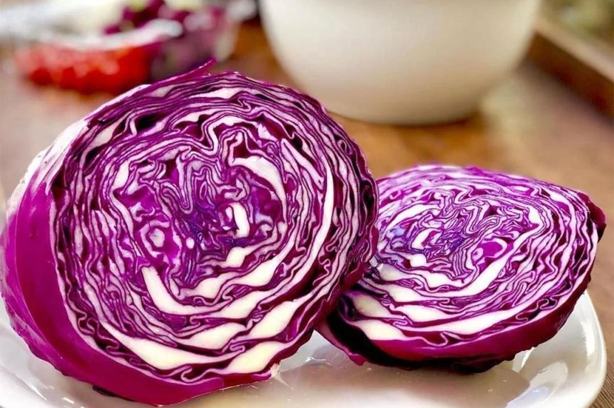 Two halves of a vibrant red cabbage sitting on a white plate, showing the striking purple and white patterns of the layered interior leaves.