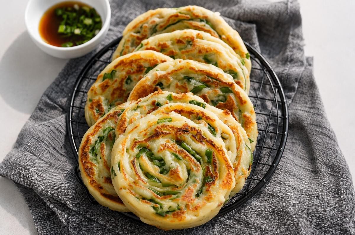 Flaky scallion pancakes coiled on a wire rack served with soy dipping sauce.
