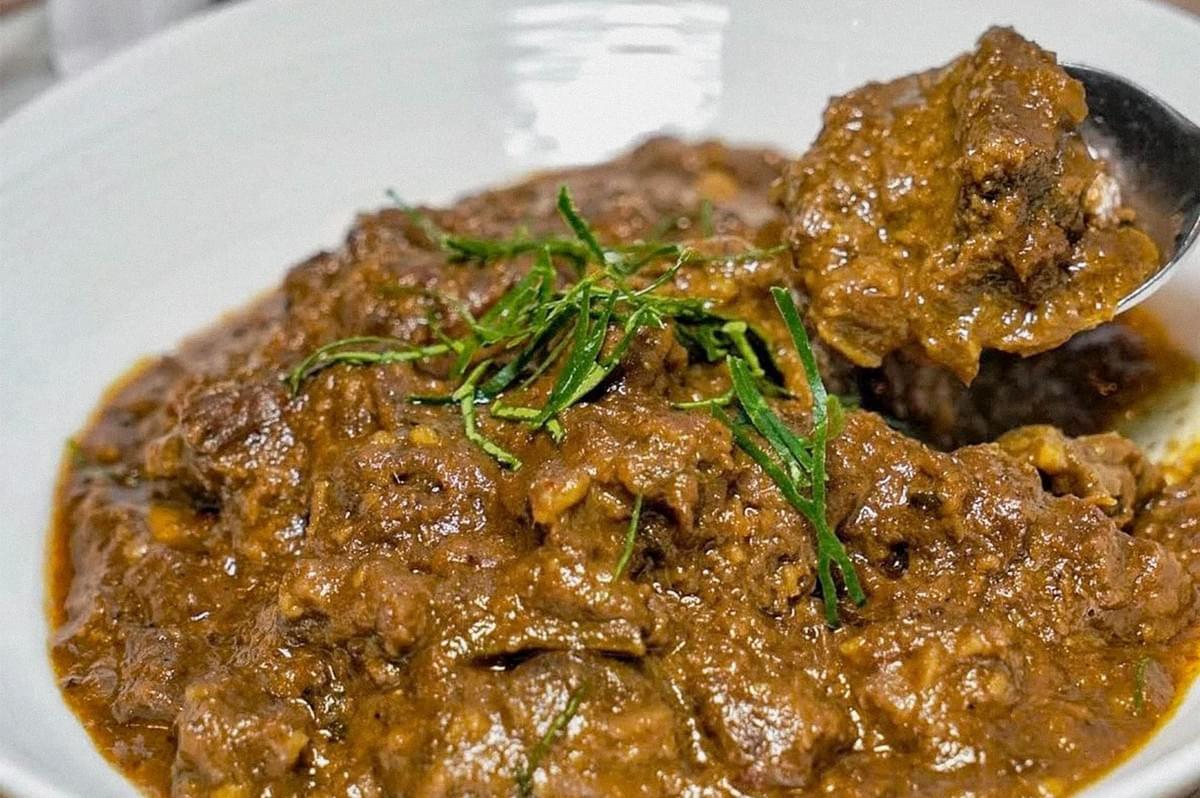 A plate of tender beef pieces coated in a thick, brown spiced sauce and garnished with thinly sliced green herbs.