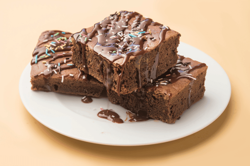 A stack of rich chocolate brownies drizzled with syrup and sprinkles, showcasing a dense, fudgy texture ideal for comparing baking styles.