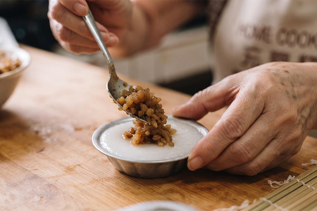 Person adding chai poh topping to freshly steamed chwee kueh in a small mould.