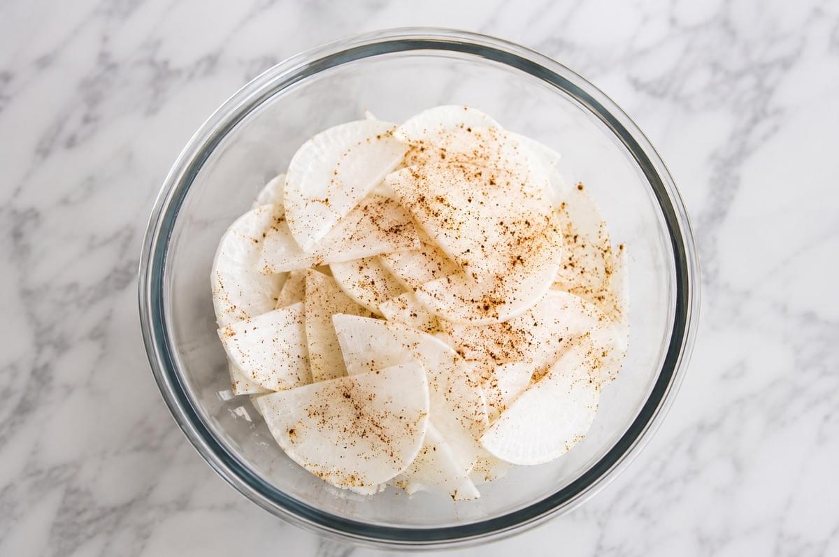 Thinly sliced white radishes tossed with spices in a glass bowl.