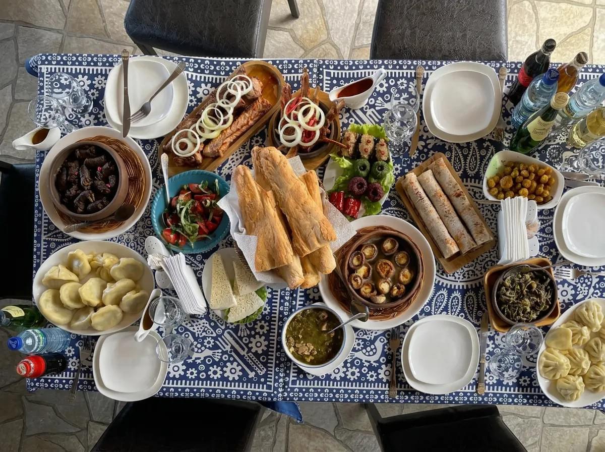 A top-down view of a traditional Georgian feast on a patterned tablecloth, featuring khinkali, bread, and side dishes.