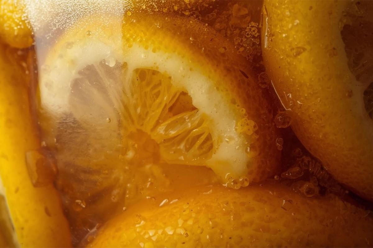 Extreme macro view of preserved lemon slices soaking in a brine or liquid inside a glass jar, showing the texture and bright yellow color.