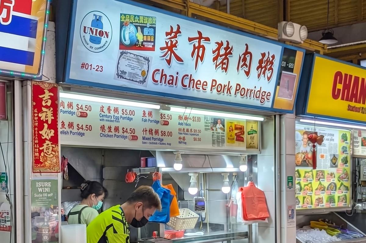Chai Chee Pork Porridge hawker stall in Singapore featuring a blue and white signboard, Chinese characters, a price menu for century egg and chicken porridge, and staff wearing face masks.