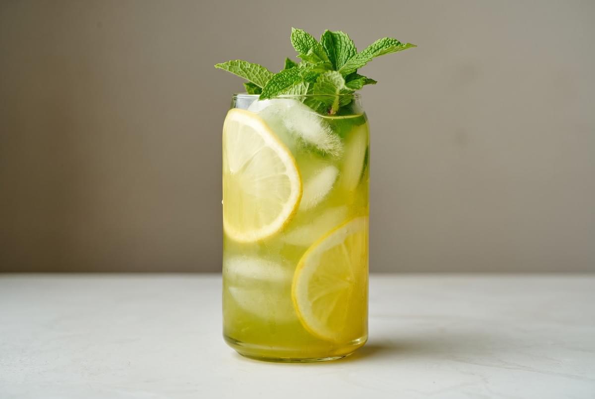 Tall glass of iced green tea or lemonade garnished with lemon slices and a bundle of fresh mint leaves.