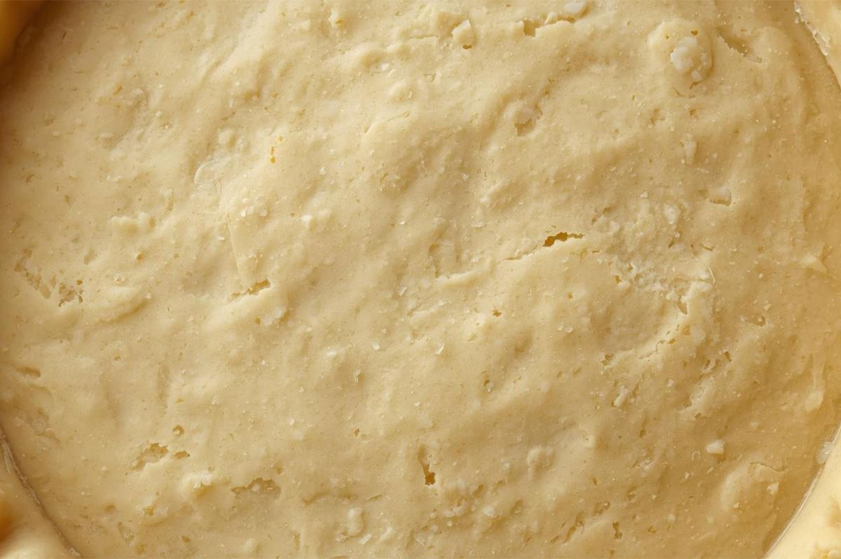 Close-up texture shot of unbaked, rough shortcrust pastry pressed into a circular pie pan, showing visible flakes of butter throughout the dough.