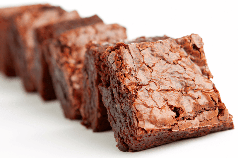 A diagonal lineup of glossy, cracked-top brownies with a dense, moist interior—classic indicators of cakey technique.