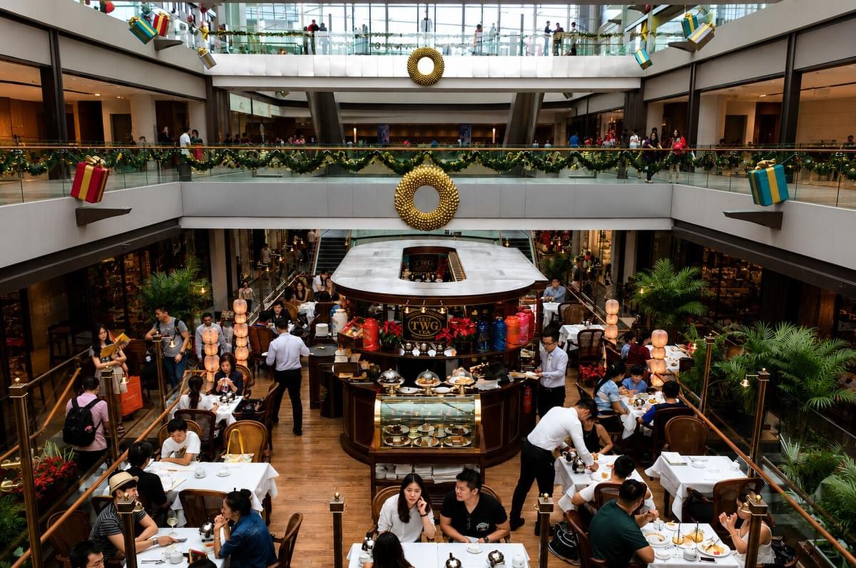 An overhead view of a busy TWG Tea salon set in the central atrium of a multi-level luxury shopping mall decorated for Christmas.