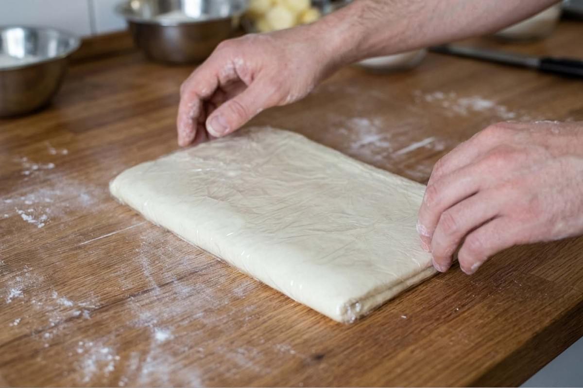Hands folding wrapped dough on a floured wooden board