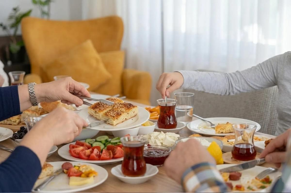 People enjoying a communal Turkish breakfast, serving börek pastry and drinking tea from traditional tulip-shaped glasses