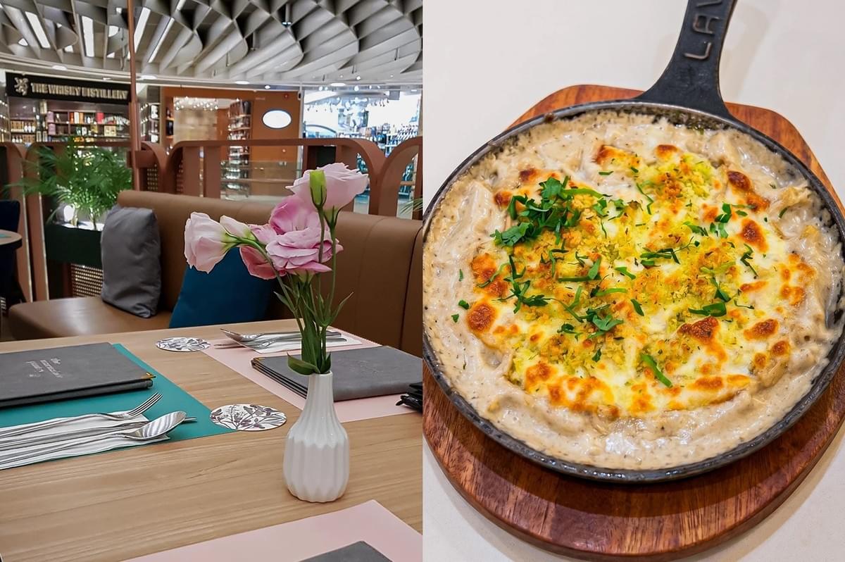 Left: An eye-level, three-quarter view of a restaurant dining table set with placemats, menus, and silverware, highlighted by a small white textured vase holding fresh pink carnation flowers, with brown booths, throw pillows, and a retail mall interior blurred softly in the background. Right: A top-down, close-up shot of a baked pasta or gratin dish served sizzling hot in a black cast-iron skillet on a round wooden trivet, showing a bubbling, creamy sauce topped with a golden-brown melted cheese crust, breadcrumbs, and a garnish of freshly chopped green herbs.