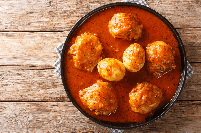 A top-down overhead view of Doro Wat in a round black dish, with chicken pieces and whole boiled eggs arranged in a rich, thick Ethiopian spiced stew.