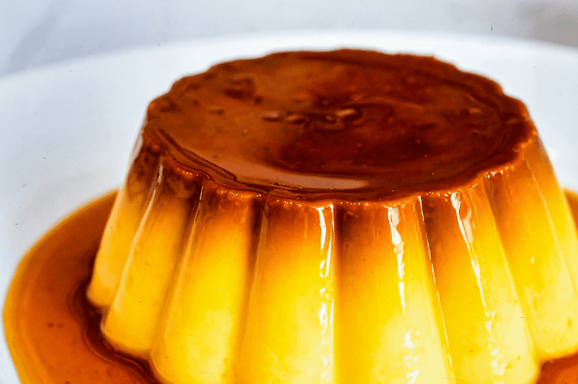 Close-up of a fluted flan mold showing a rich, dark caramel glaze dripping down the textured sides of the golden custard.
