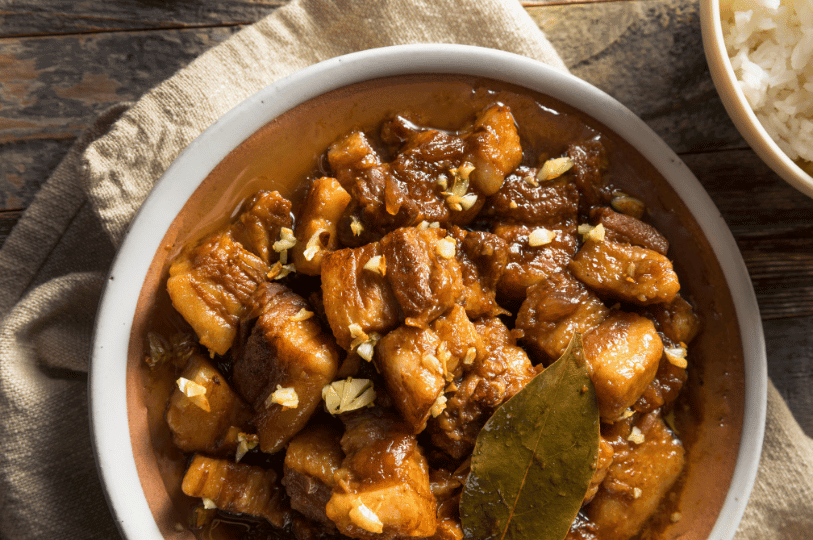 Overhead view of a plate of Pork Adobo with a side of white rice, emphasizing the "saucy" consistency and the contrast between the dark meat and the white rice.