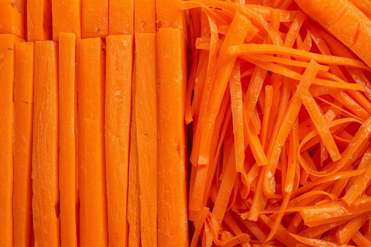 A macro, split-screen shot showing two different carrot cuts: thicker, rectangular batonnet sticks on the left, and very thin, finer julienne cuts on the right.
