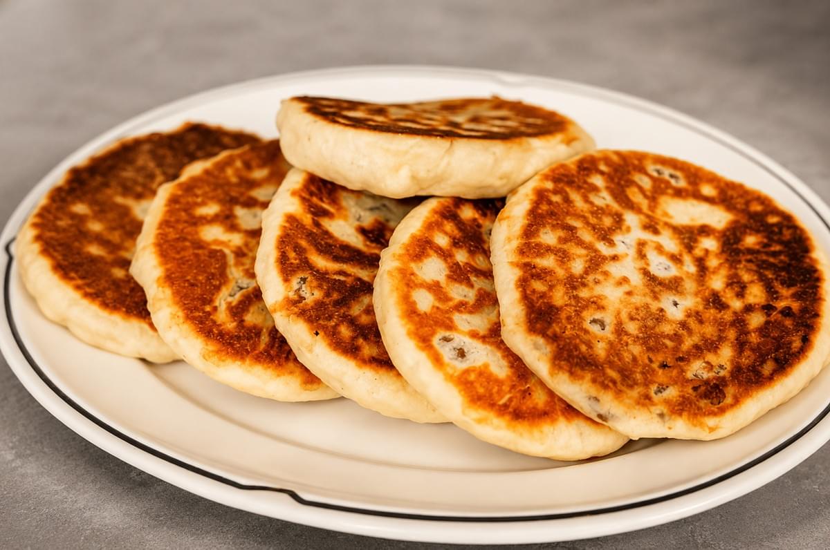 A row of golden, pan-fried hotteok pancakes arranged on a oval white serving plate.