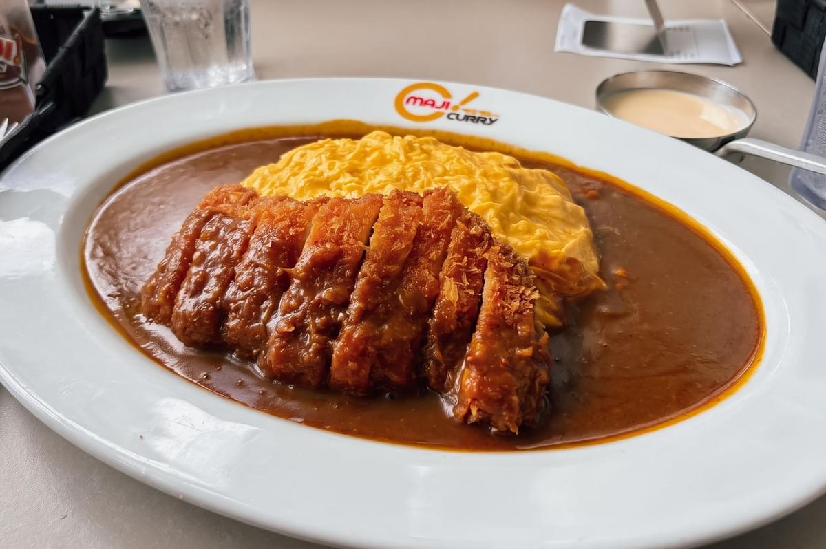 Close-up of Maji Curry’s Japanese curry topped with sliced crispy pork cutlet and fluffy scrambled eggs, served on a large white plate with curry sauce.