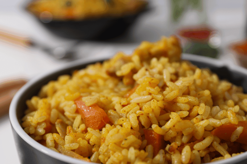A close-up shot focusing on the rich texture of yellow-tinted rice and soft, cooked orange carrots in a bowl of aromatic pilaf.