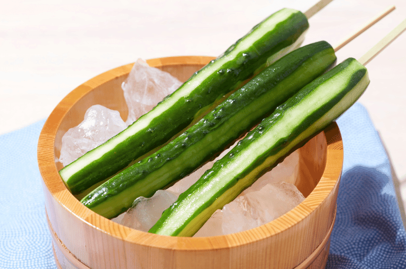 A refreshing glass of iced water infused with thin slices of fresh green cucumber and sprigs of mint, set against a bright, summery background.