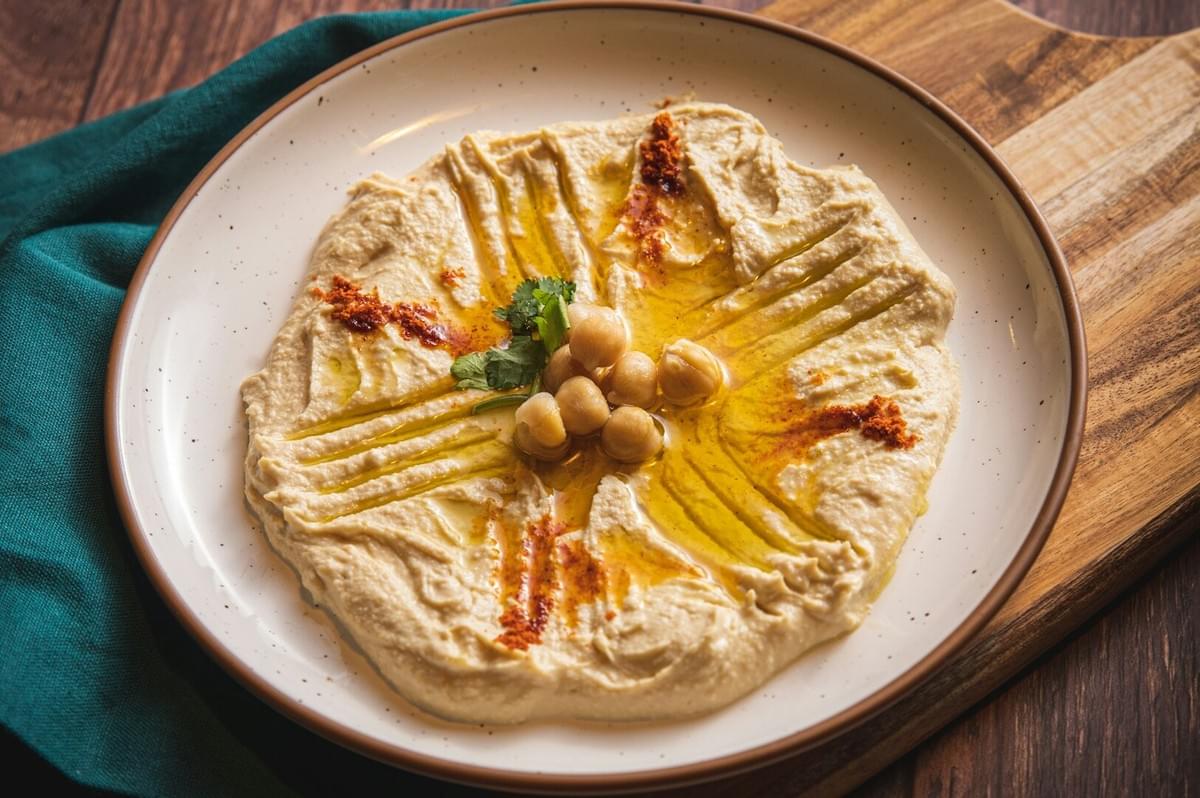 Smooth and creamy hummus drizzled with olive oil and topped with herbs on a white plate.