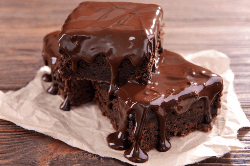 Three stacked brownies with dripping chocolate glaze and embedded chunks, styled to highlight fudgy richness.