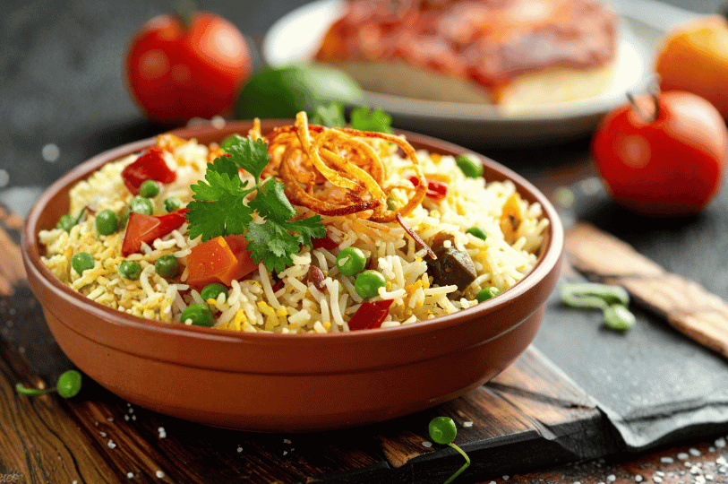 A rustic terracotta bowl of mixed rice with diced carrots and green peas, beautifully crowned with a nest of crispy fried onions and a sprig of cilantro, resting on a wooden board.