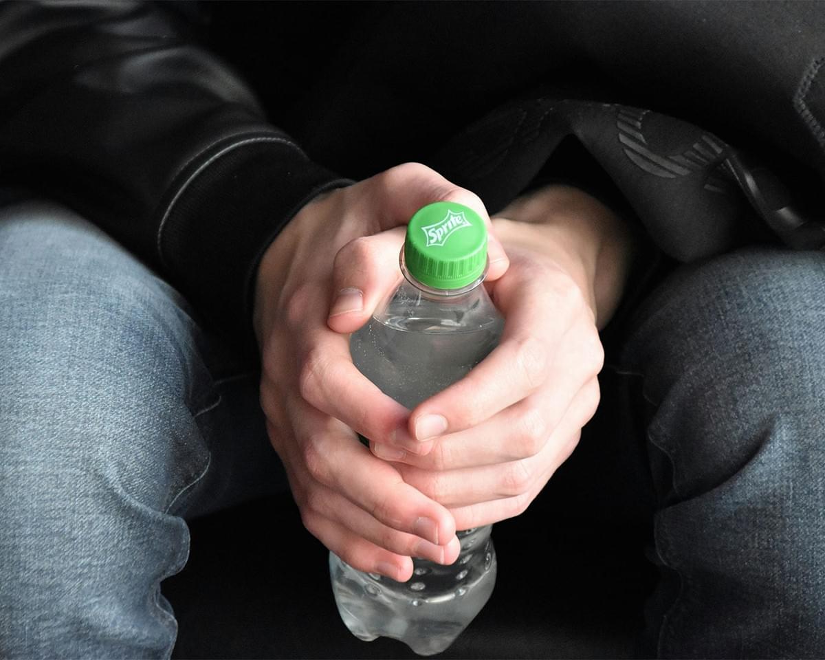 A close-up of a hand holding a clear bottle of water, symbolising refreshment and hydration in a warm outdoor setting.