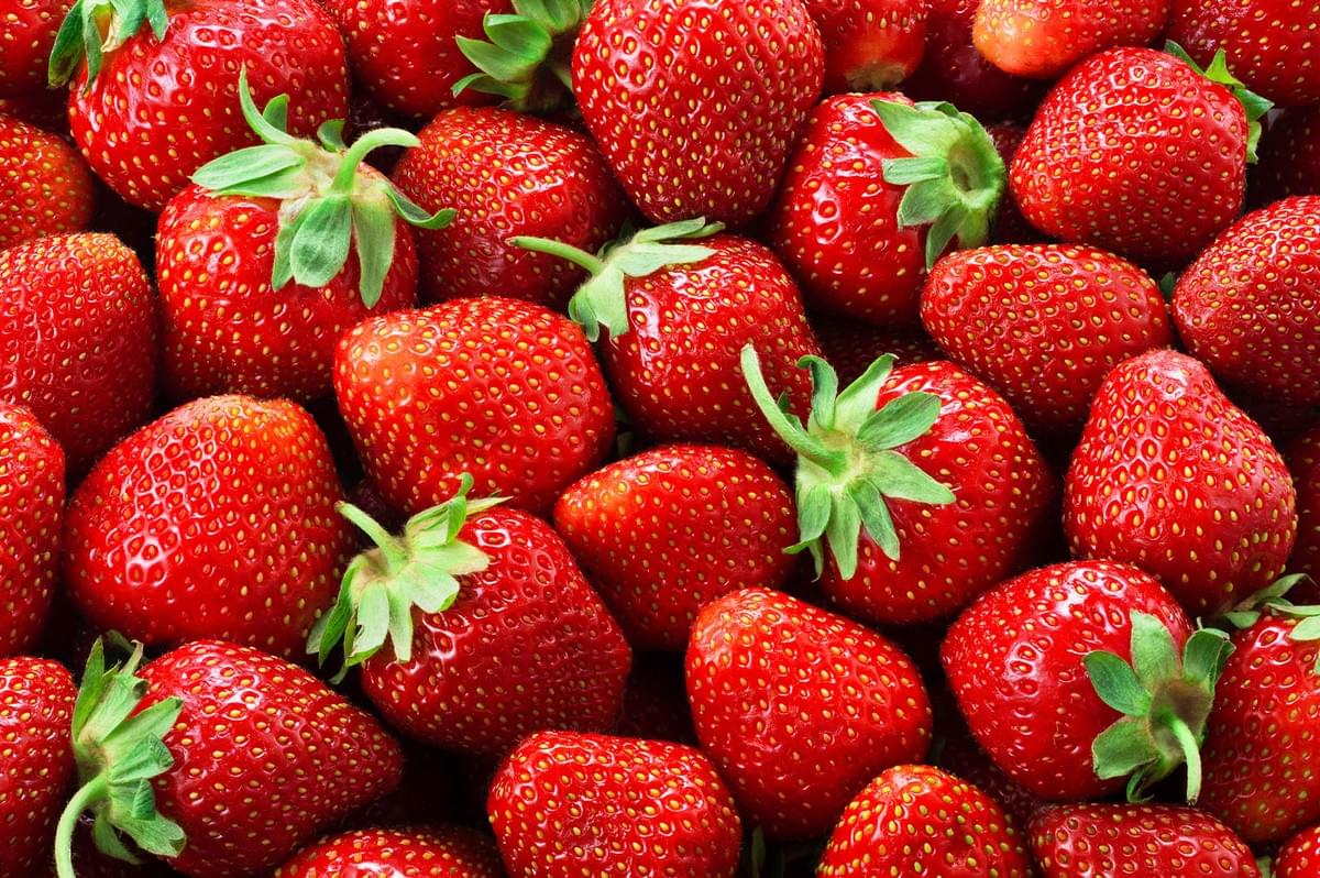 A vibrant, close-up overhead shot of a pile of freshly picked, red, ripe strawberries covering the entire frame.