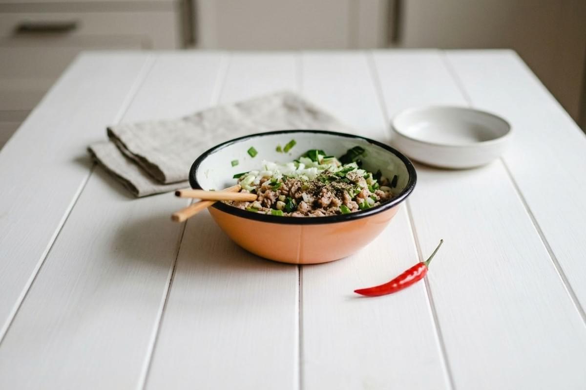 A bowl of authentic Laotian Larb featuring minced meat and herbs, served with chopsticks and a red chili on a white table