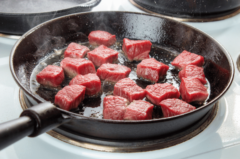 Small cubes of beef chuck searing in a hot pan, demonstrating the importance of spacing meat to ensure proper browning rather than steaming.