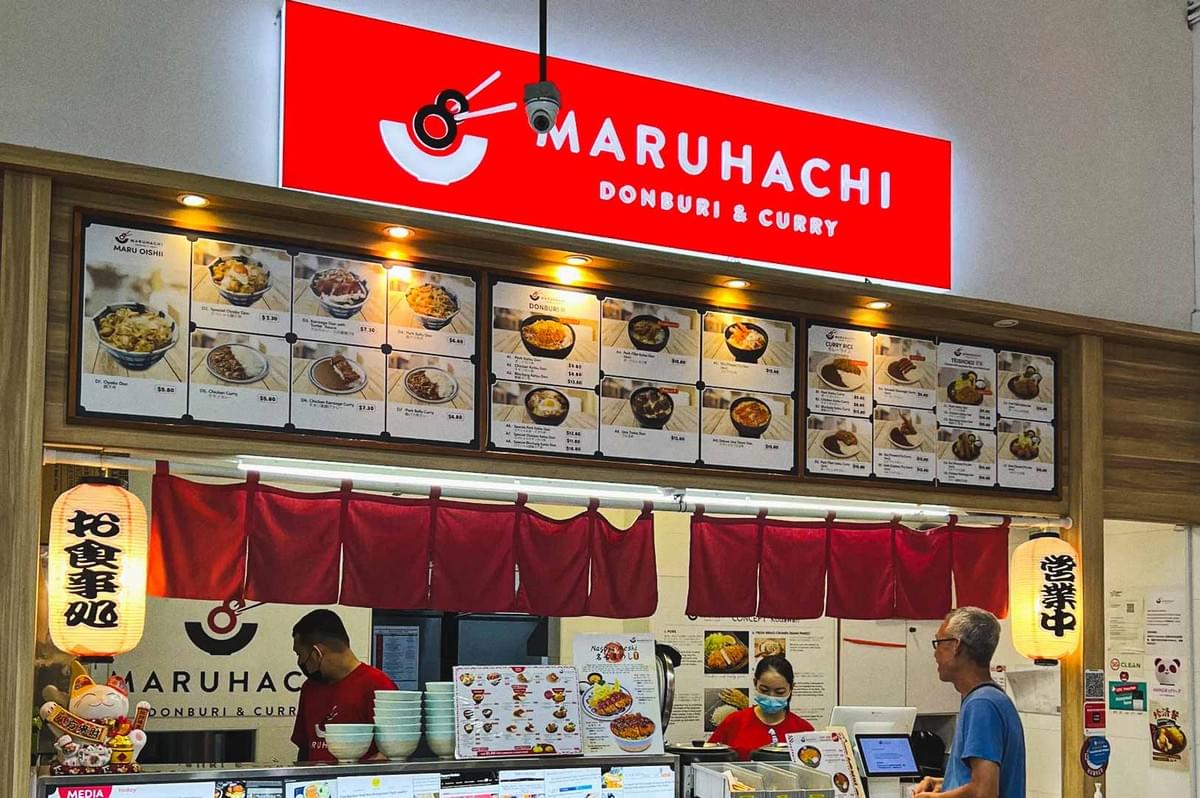 Maruhachi Donburi & Curry food stall with a bright red signboard, Japanese-style curtains, and a menu display featuring various donburi and curry dishes.