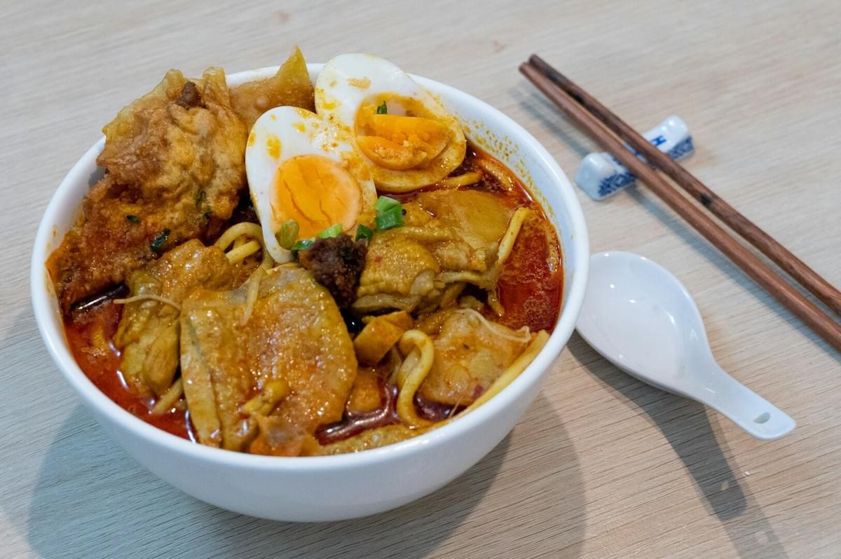 A bowl of Laksa featuring chicken and noodles, accompanied by a pair of chopsticks resting on the side.