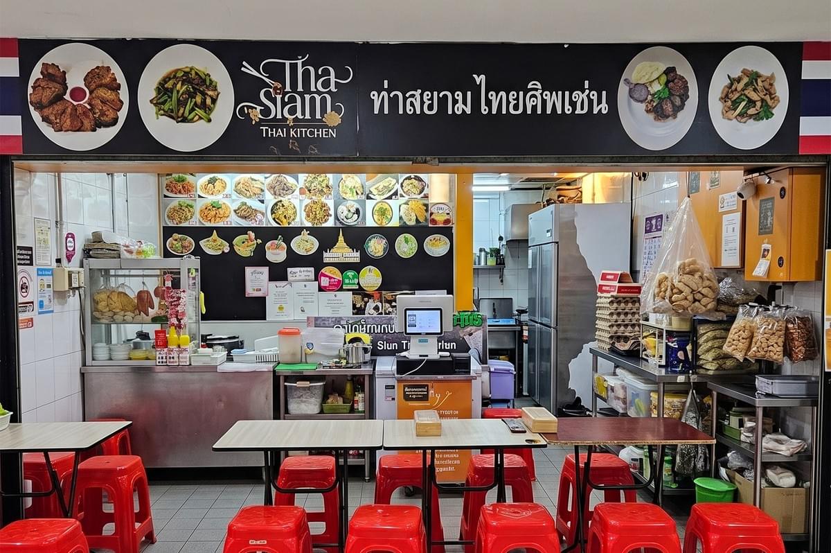 Tha Siam Thai Kitchen restaurant storefront with red stools, menu displays, and outdoor seating.