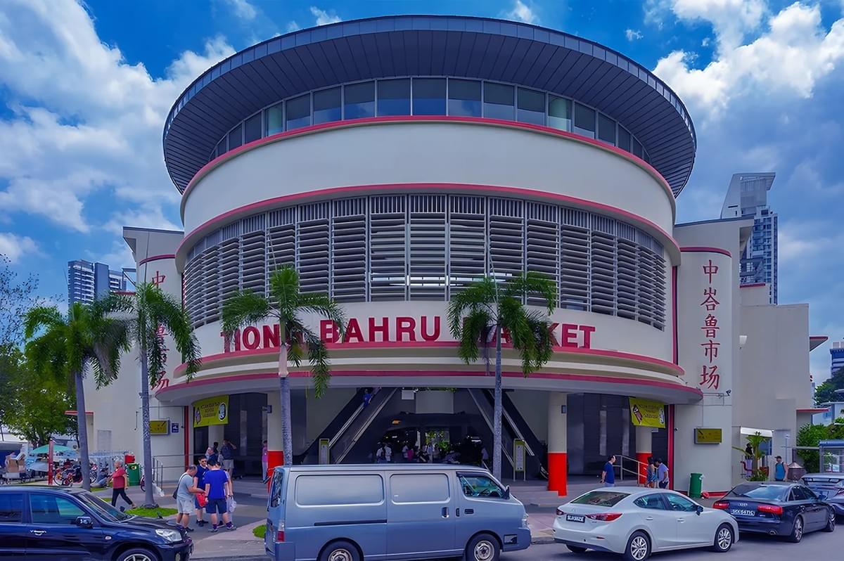 Circular building marked as Tiong Bahru Market with art deco architecture, palm trees, and a busy street. Skies are blue with white clouds.