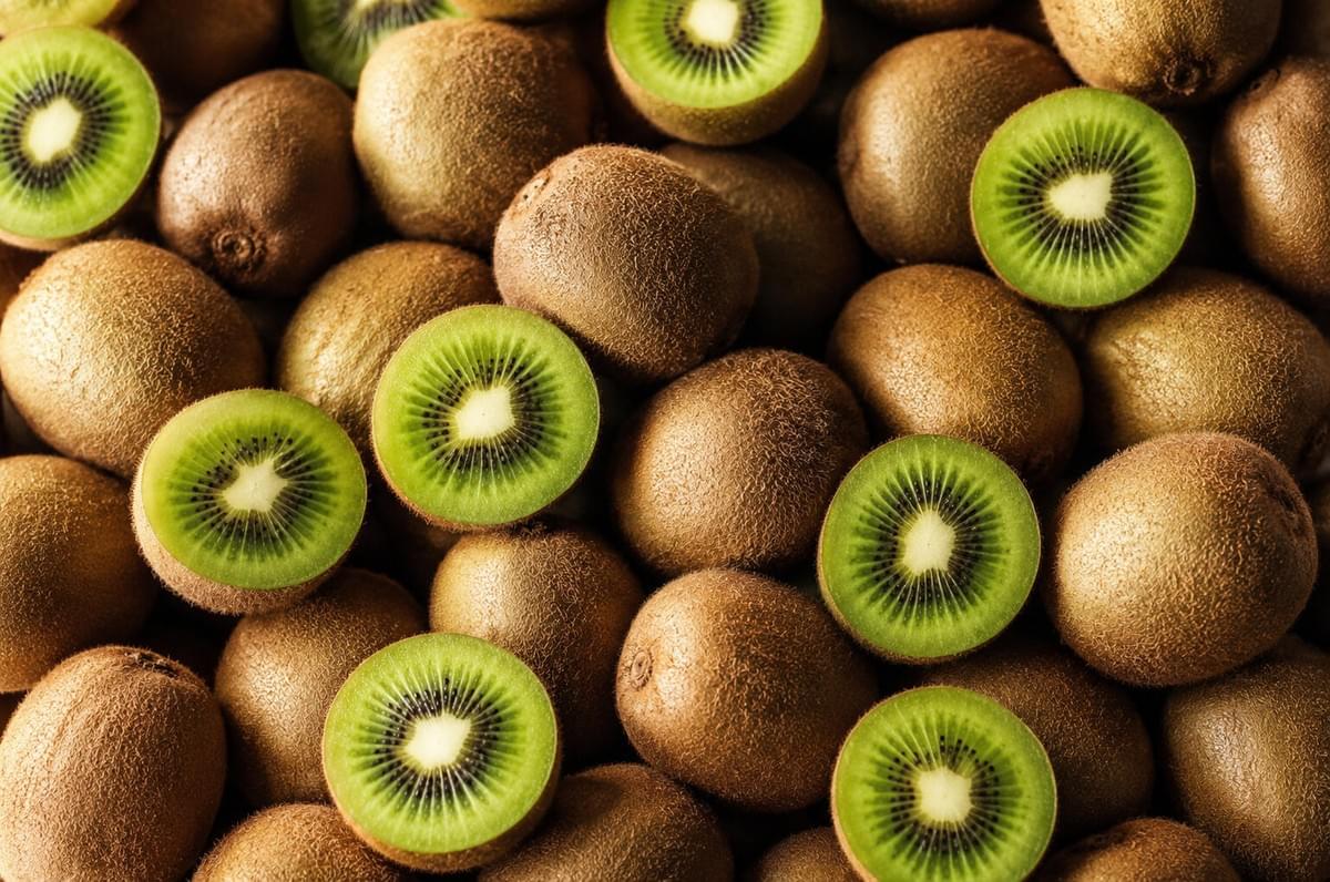 Flat lay of fresh whole kiwifruits mixed with several cross-cut halves revealing their green seeds.