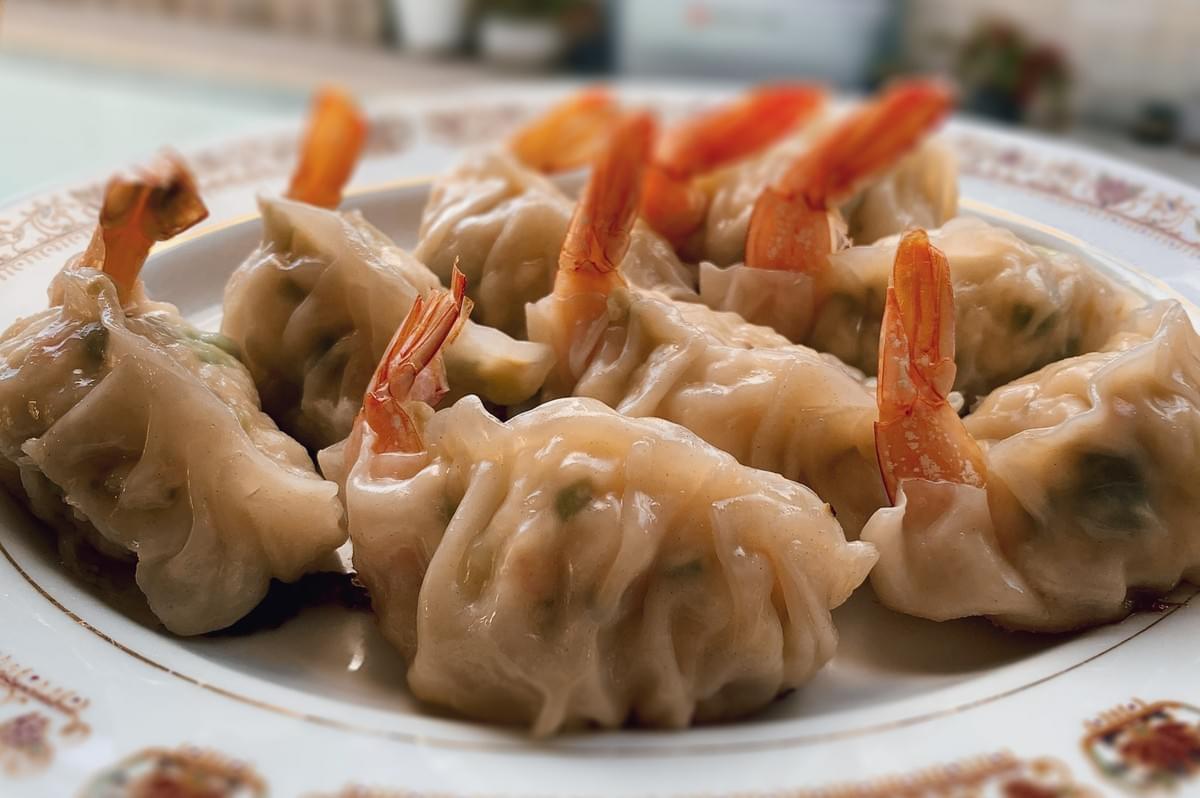 Plate of freshly steamed shrimp dumplings arranged on a decorative dish, highlighting glossy wrappers and vibrant shrimp tails.