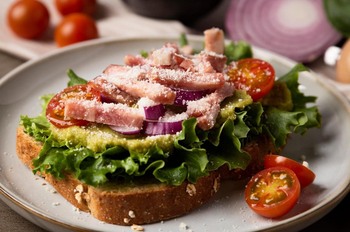A Nordic open sandwich featuring layers of bacon, lettuce, tomatoes, and avocado, highlighting a colorful and appetizing presentation.