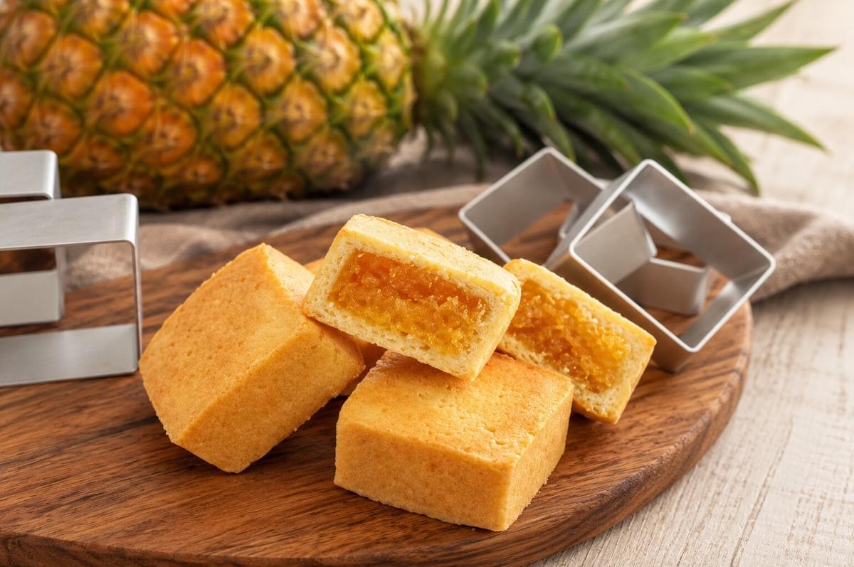 Pineapple cakes arranged on a white plate with overflow pieces served inside a hollowed-out pineapple shell.