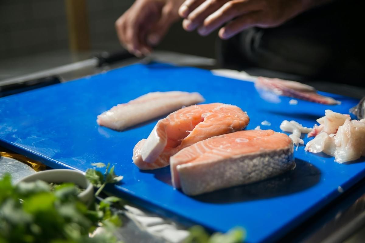  This close-up image features two thick, fresh-looking salmon steaks positioned on a bright blue cutting board, alongside a smaller, pale white fish fillet and some fish trimmings.