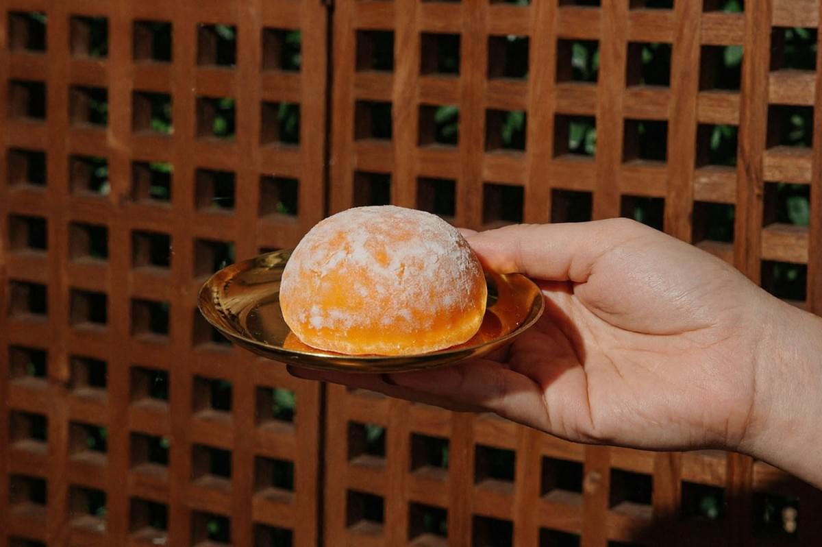Orange mochi dusted with powdered sugar on golden plate held against wooden lattice background