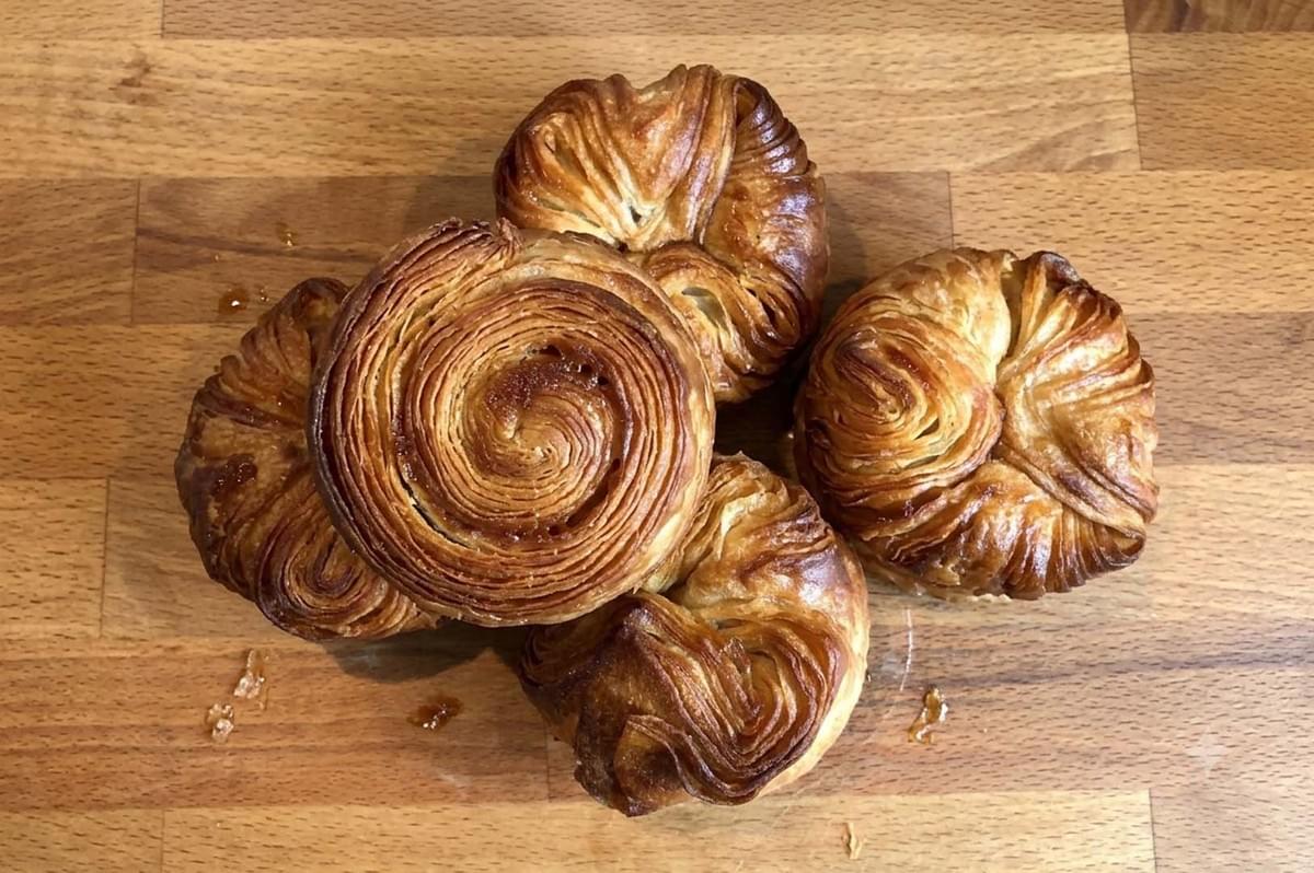 Four spiral-shaped Kouign-Amann pastries on a wooden board