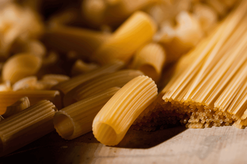 Close-up of dried pasta varieties featuring thick, ridged tubes, such as rigatoni or maccheroni, resting beside a neat bundle of long spaghetti strands.
