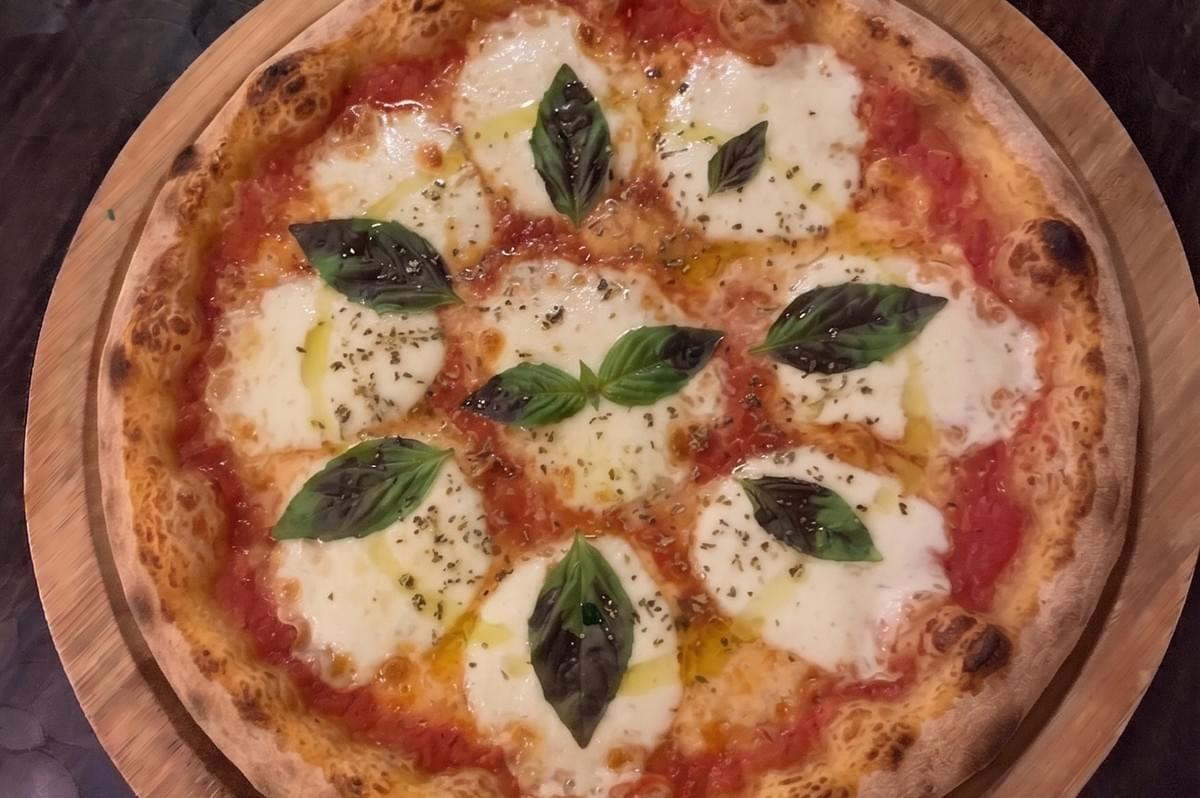 Freshly baked traditional Margherita pizza with melted mozzarella cheese and basil leaves on a wooden pizza peel.