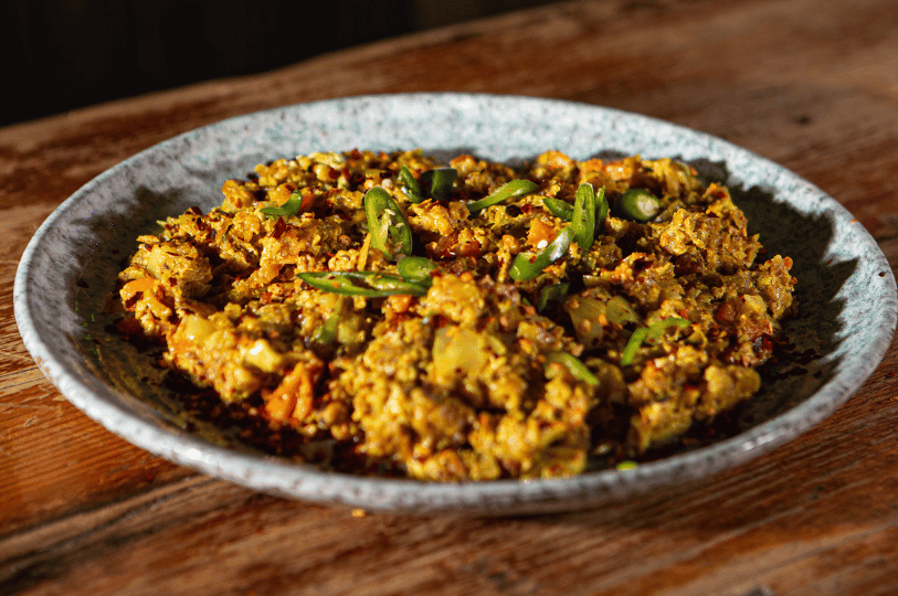 A close-up of a vibrant yellow Kottu Roti topped with fresh sliced green chilies, highlighting the finely chopped texture of the flatbread.