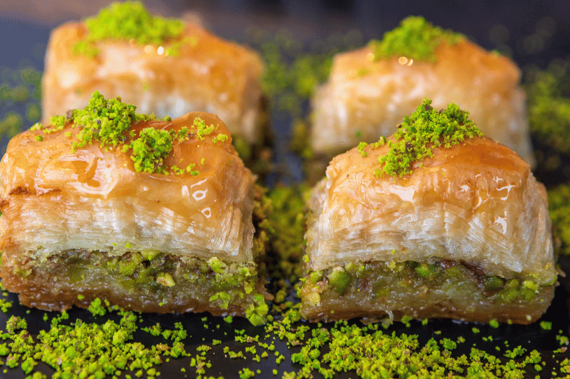 A close-up side view of four pieces of baklava, highlighting the many thin, flaky layers of phyllo dough separated by a thick layer of crushed green pistachios.