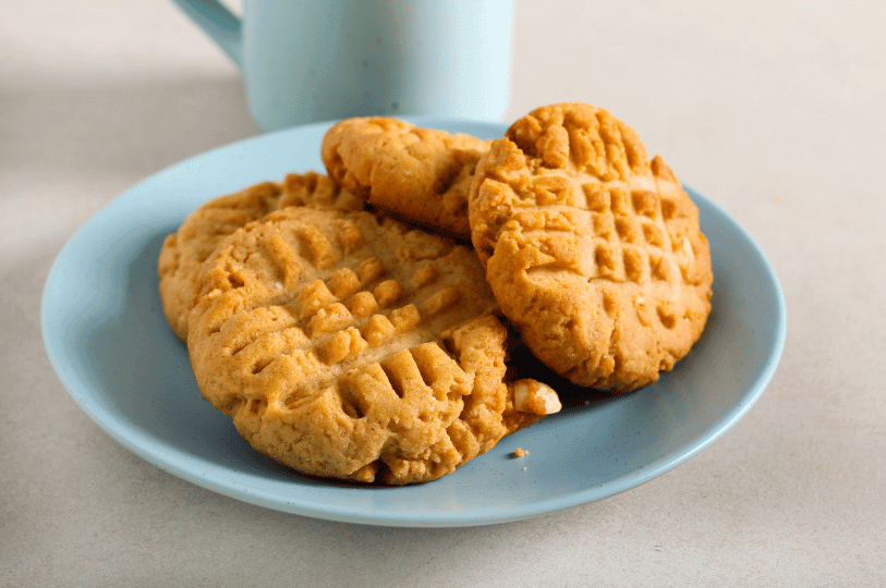 A bright, clean shot of three peanut butter cookies resting on a white plate, emphasizing the simple, rustic aesthetic of the three-ingredient recipe.
