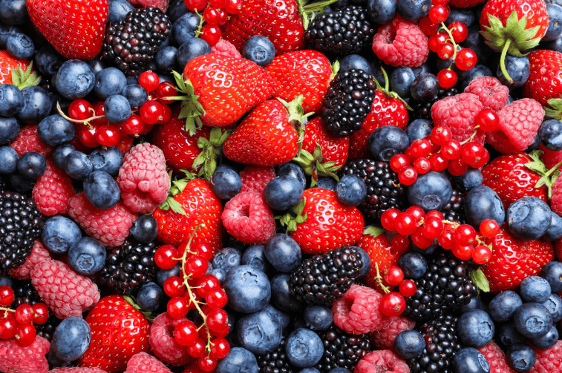 A dense, colorful overhead view of assorted berries, including bright red currants on the stem, blackberries, and blueberries, showing the variety of textures used in mixed-berry preserves.