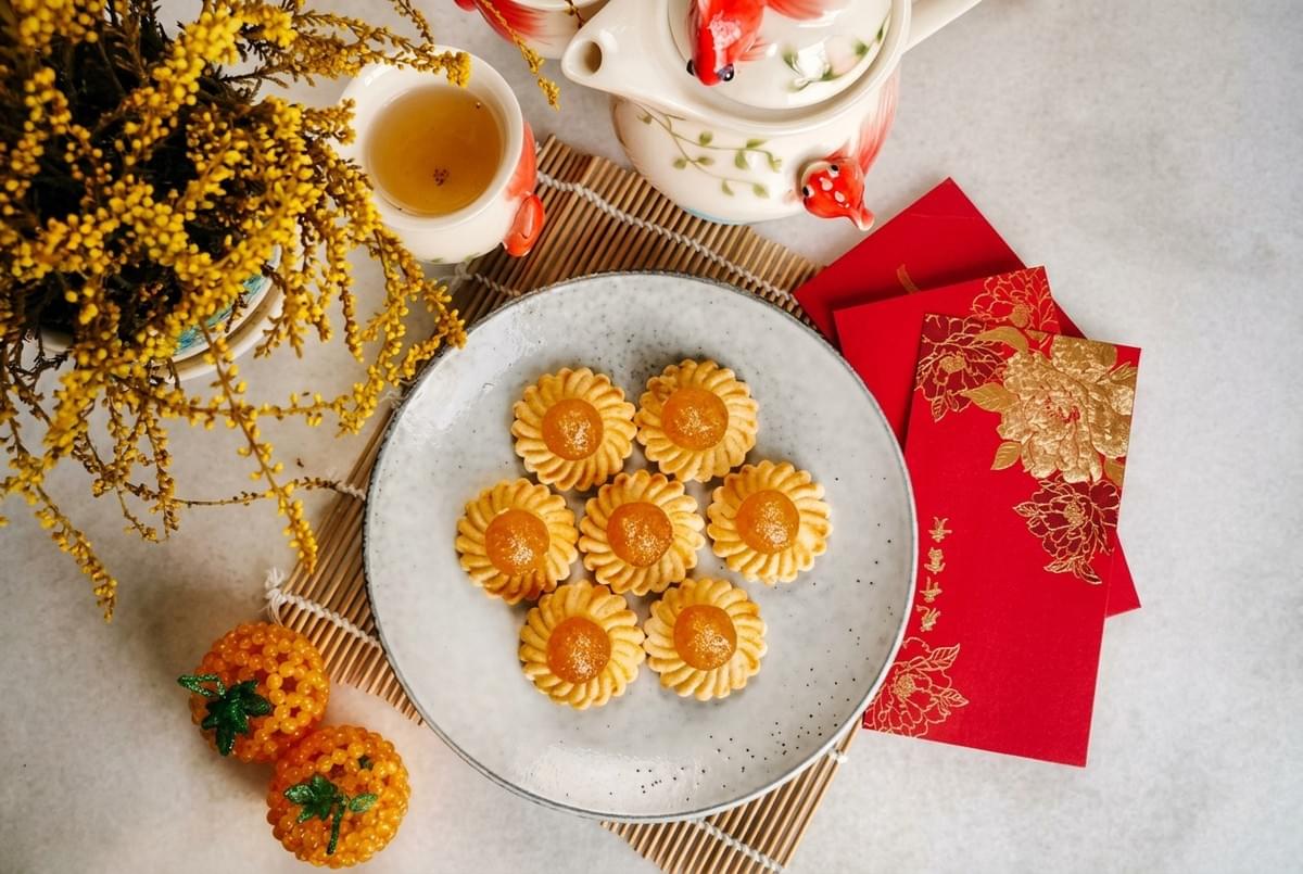 Open-faced pineapple tarts served on a plate alongside red envelopes and a teapot.  