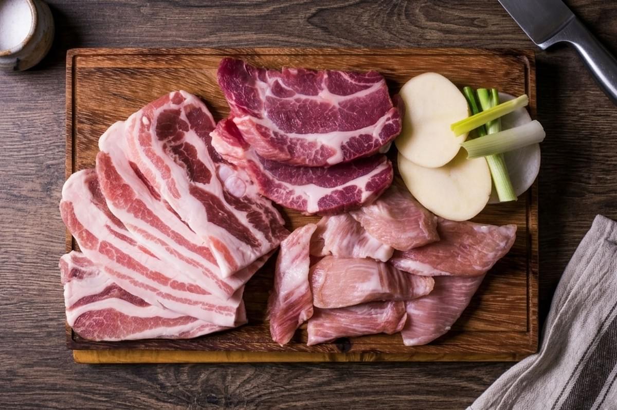 Raw pork cuts and aromatics on a wooden board, the primary ingredients for preparing Laotian Larb
